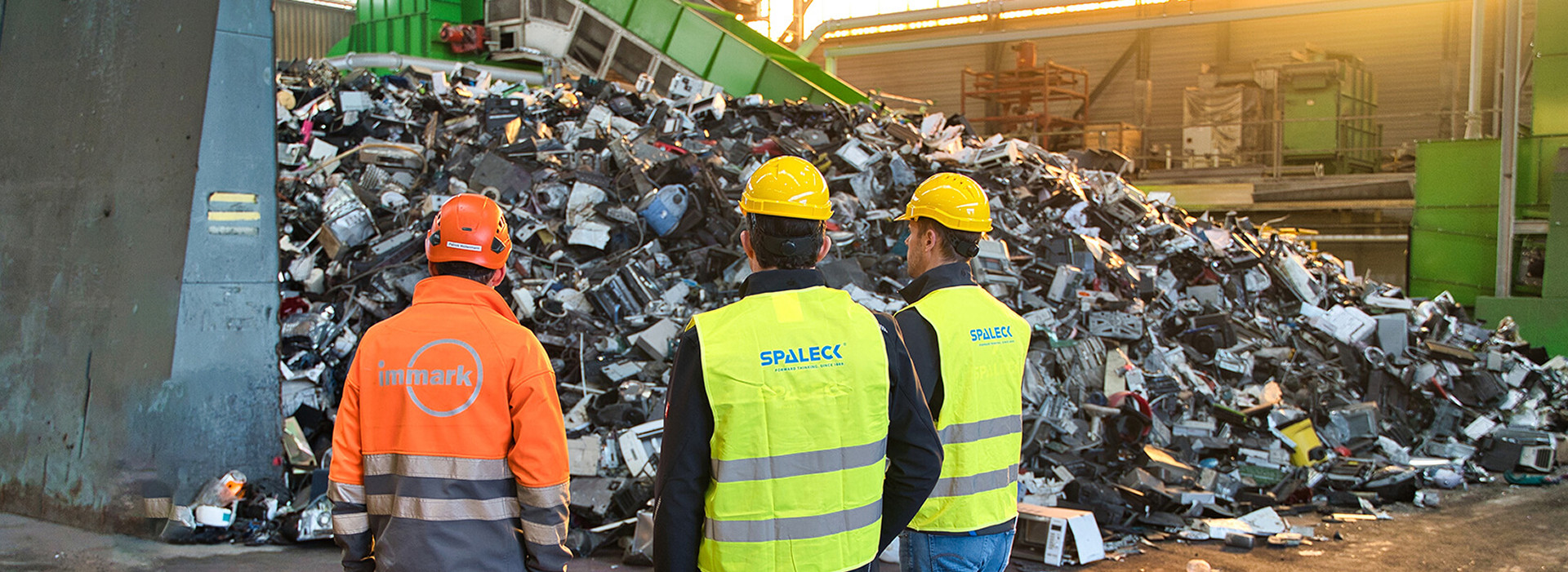 Trabalhadores perante uma grande pilha de resíduos eletrónicos numa unidade de reciclagem.