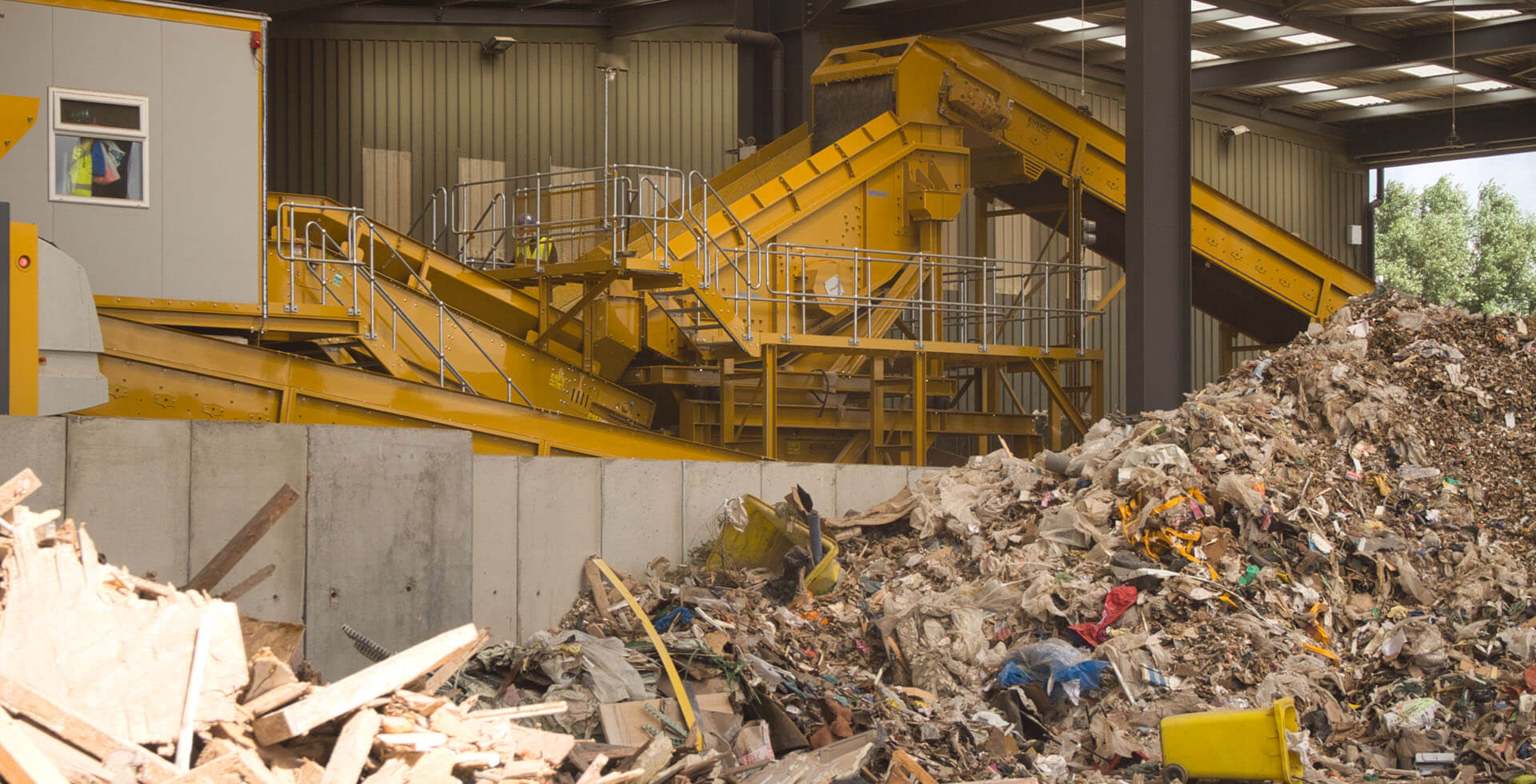 Instalação de reciclagem de resíduos mistas da construção, com correias transportadoras e pilhas de resíduos.