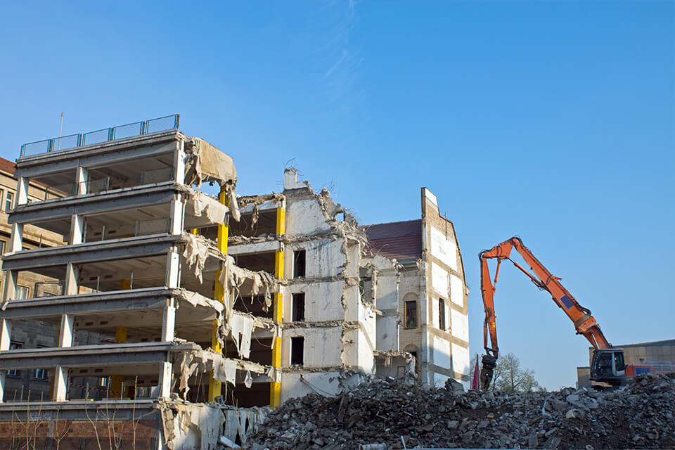 Demolição de um edifício com uma escavadora, com resíduos de construção em primeiro plano.