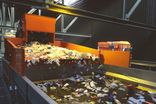 A calha transportadora oscilante encaminha o material reciclável proveniente de embalagens leves para um equipamento de triagem por infravermelhos (NIR). O material é bem distribuído por toda a largura, o que constitui um fornecimento ideal.