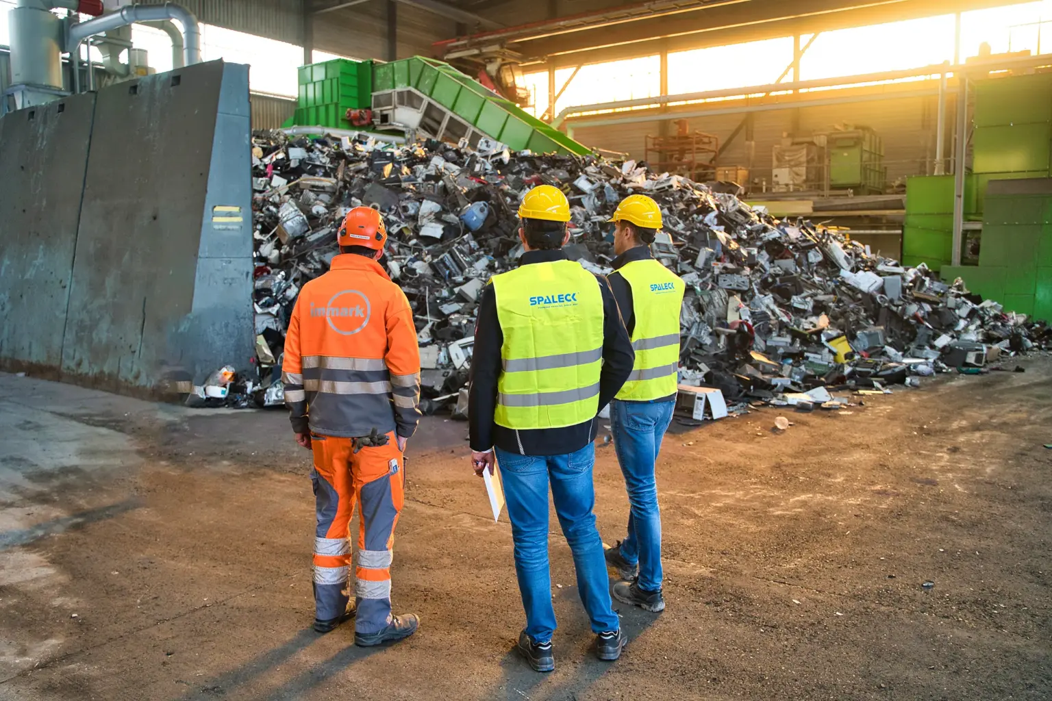 O gestor de projeto da Immark e dois especialistas em máquinas de crivagem da SPALECK estão perante o material de entrada não triturado destinado à nova instalação de tratamento de resíduos eletrónicos