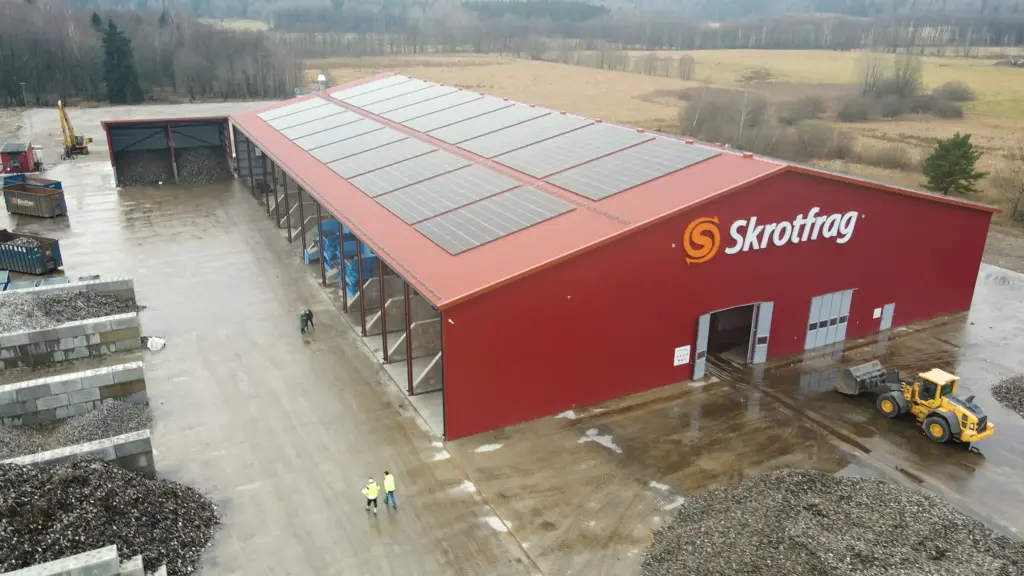 Unidade de reciclagem Skrotfrag para metais não ferrosos, com um edifício vermelho e painéis solares.
