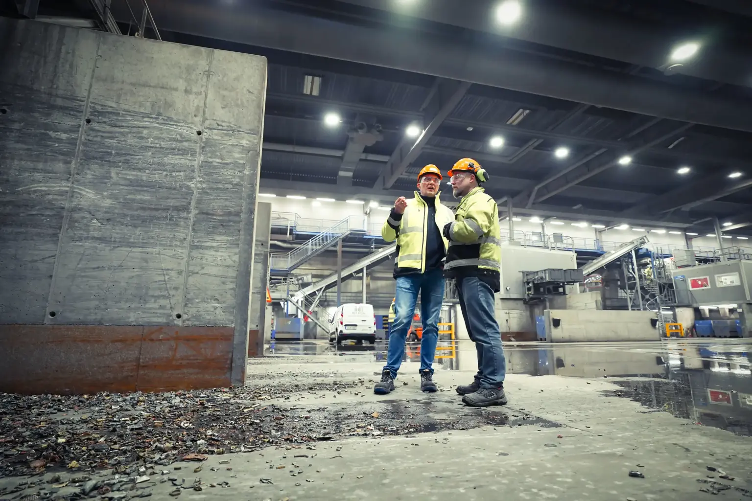 Dois trabalhadores com equipamento de proteção estão a conversar num pavilhão industrial.