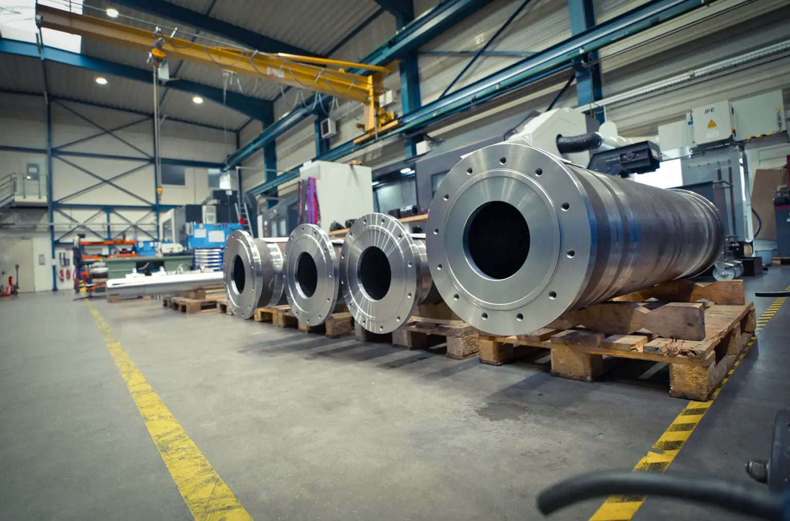 Grandes cilindros metálicos em paletes numa oficina de usinagem CNC de peças de grandes dimensões.