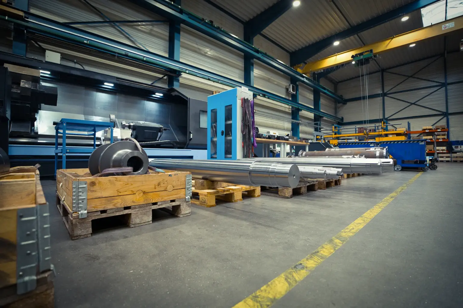 Pavilhão industrial com peças torneadas longas em paletes.