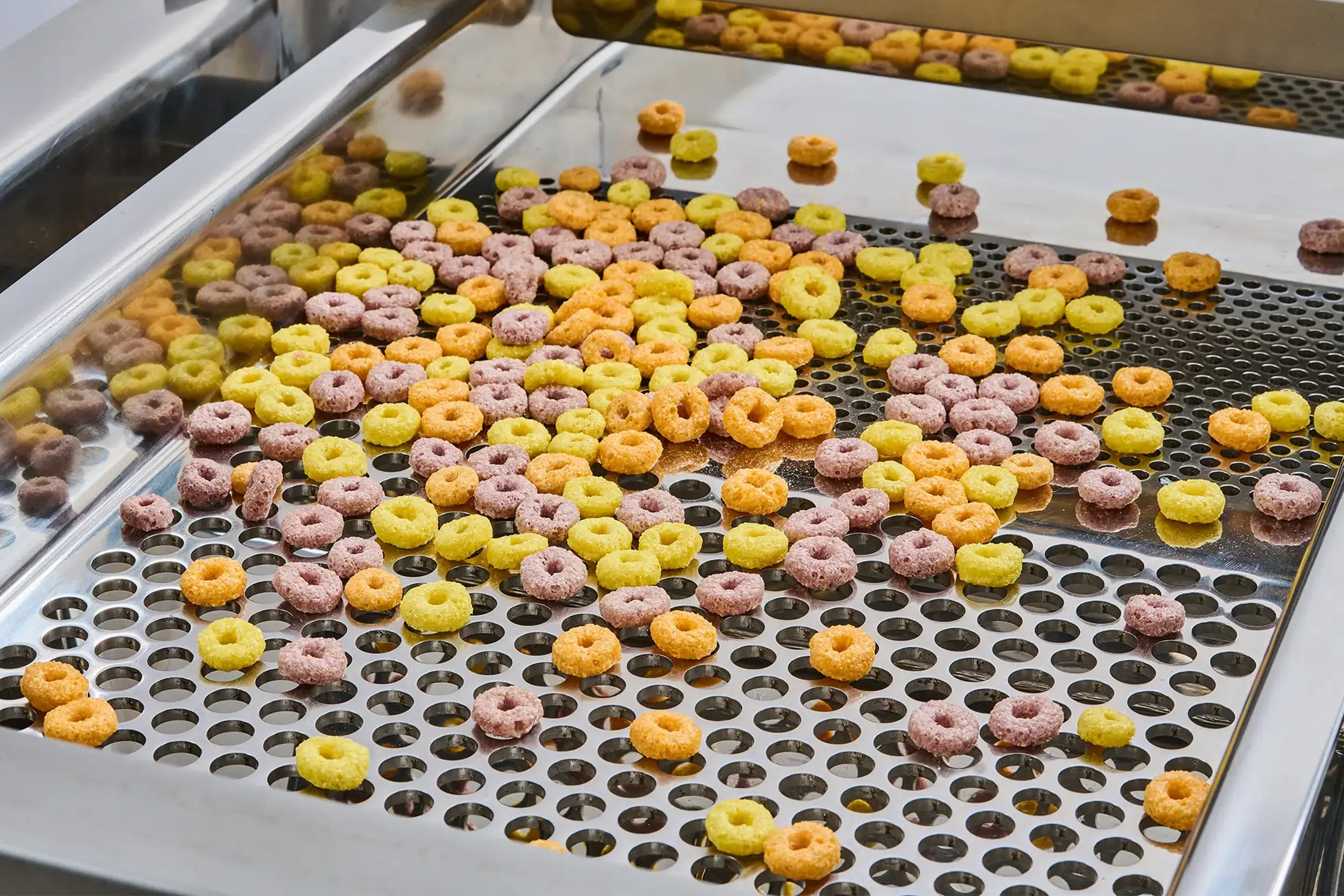 As máquinas de peneiramento de alimentos separam anéis de cereais coloridos numa peneira.