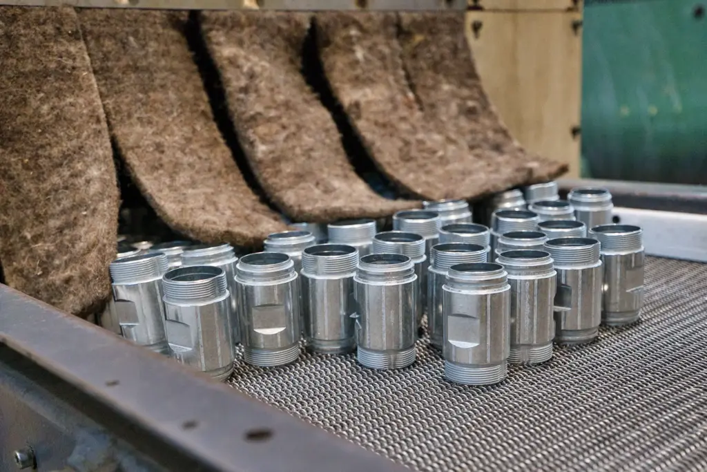 Peças metálicas numa correia transportadora, dentro de uma máquina de esmerilagem por deslizamento.