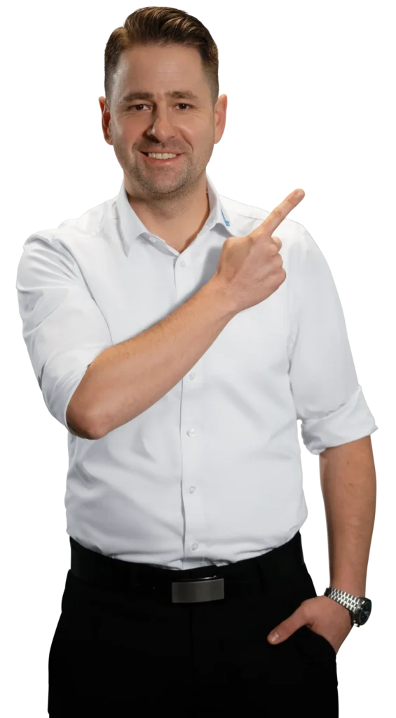 Um homem de camisa branca aponta para o lado, sorrindo.