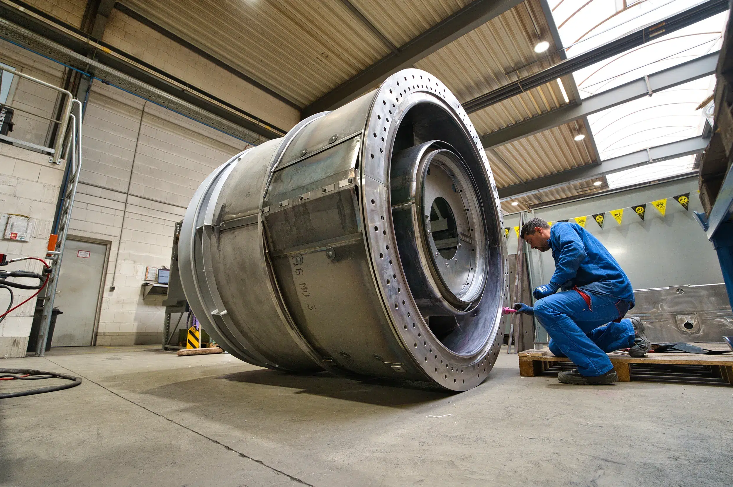 O técnico de construção da SPALECK está ajoelhado junto a um grande conjunto soldado e está a montar peças. O subconjunto faz parte de um grande subconjunto soldado destinado a uma turbina a gás. A imagem mostra a produção na SPALECK.