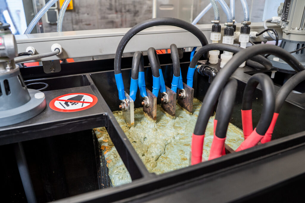 Imagem em grande plano de um equipamento de eletrocoagulação em funcionamento. Mostra as lamelas elétricas na água contaminada.