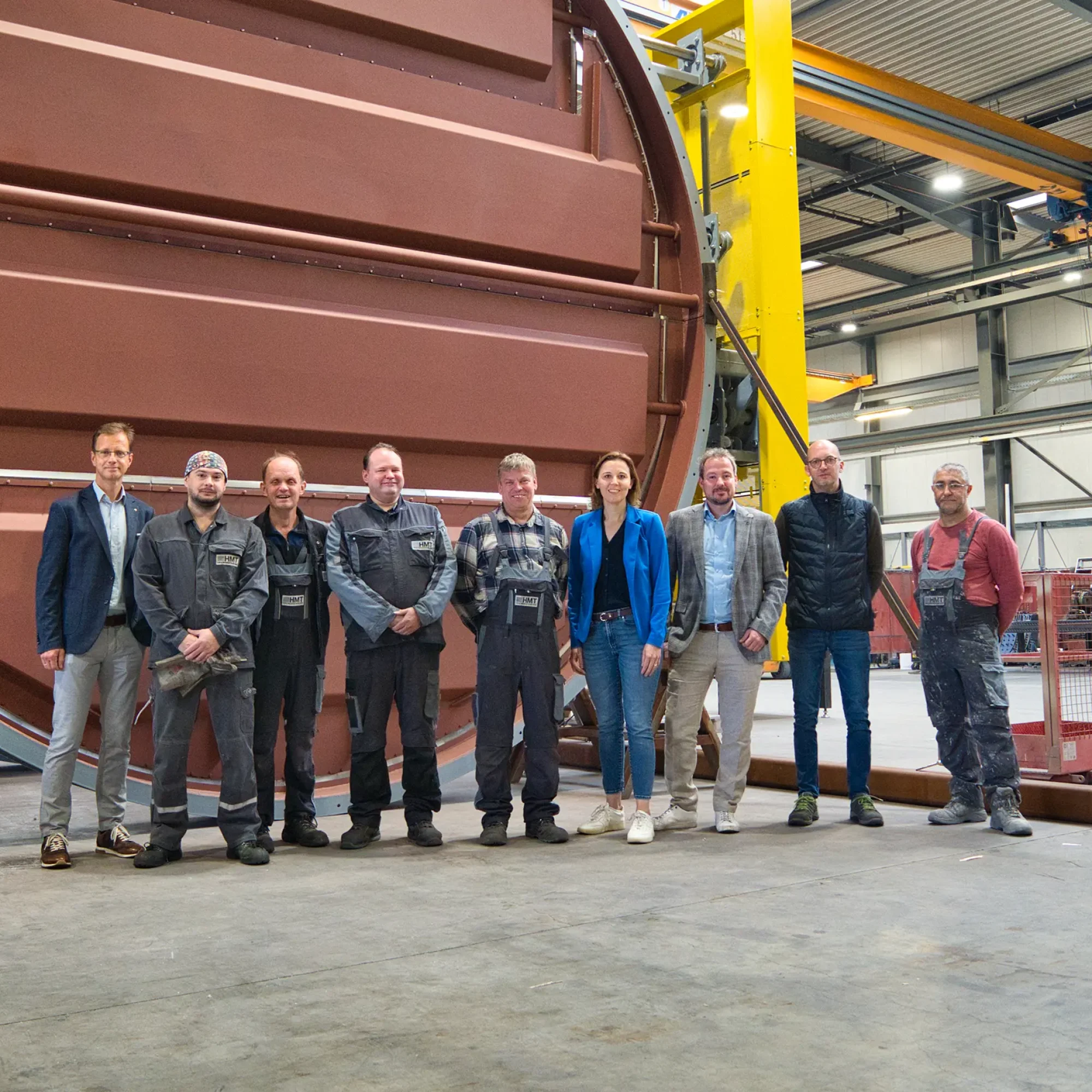 Gruppe von Menschen steht vor großer Industriemaschine in Fabrikhalle.
